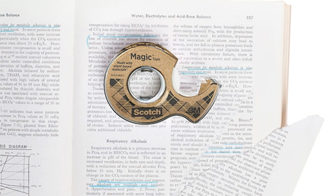 Scotch® Magic™ Tape Made with 66% Plant-based Adhesive lying on a book with a torn page
