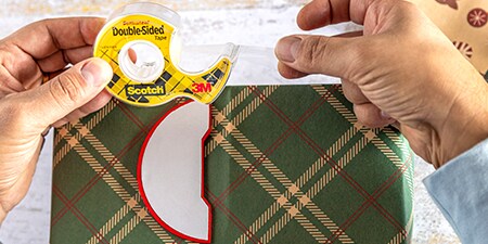 Attaching decorations to a wrapped present using Scotch® Double-Sided Tape
