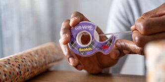 Man wrapping a gift with Scotch® Gift Wrap Tape
