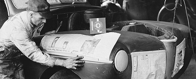 Black and white image showing a man using masking tape to avoid damaging existing paintwork for auto-body painting
